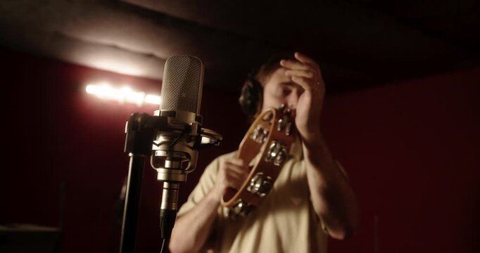 Musician with headphones playing tambourine in recording studio