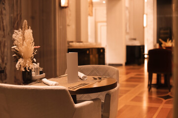 Set table with elegant chairs, blank menu, and dried flower centerpiece in a dimly lit, luxurious restaurant interior.