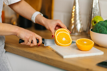 Hands cutting orange into slices on marble board in kitchen, fresh citrus for healthy breakfast and vitamin C concept.
