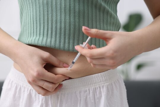 In vitro fertilisation. Woman making injection into her belly indoors, closeup