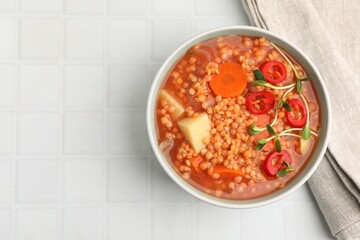 Delicious lentil soup with vegetables in bowl on white tiled table, top view. Space for text