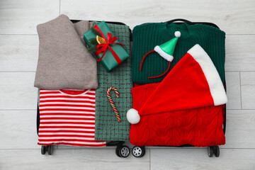 Christmas vacation. Suitcase with Santa hat, gift box and candy cane on floor indoors, top view