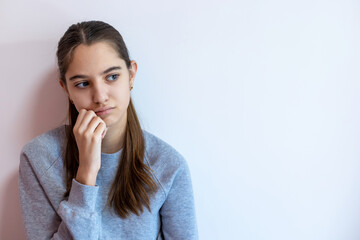 Thoughtful teenage girl looking away in silence. A teen girl wearing a gray sweater sits quietly, resting her chin on her hand while gazing away with a pensive, sad expression. Copy space.