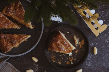 On a plate on a dark table lies a bitten piece of galette with a crown.