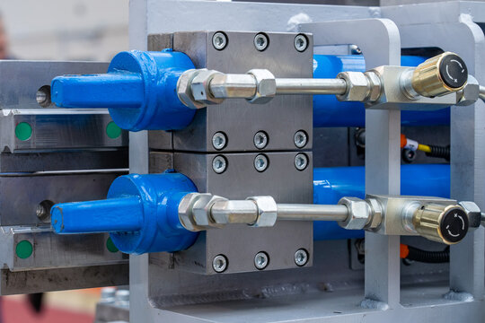 Detailed view of modern industrial machine showcasing blue hydraulic cylinders, sturdy metal blocks, interconnected pipes, and adjustable flow control valves