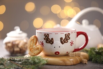 Cup of tea, cookie, sugar cubes and Christmas decor on grey table against background with blurred lights, closeup