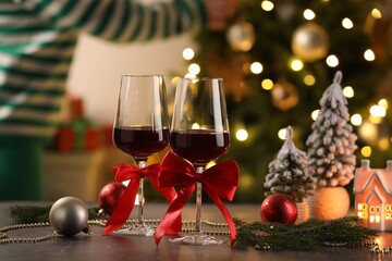 Obraz premium Glasses of red wine and Christmas decor on wooden table against background with blurred lights