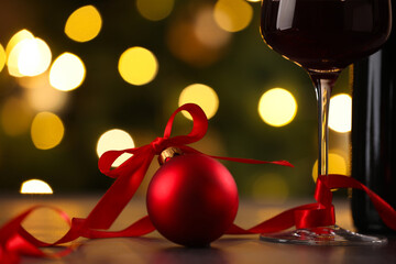 Glass of red wine and Christmas decor on wooden table against background with blurred lights, closeup