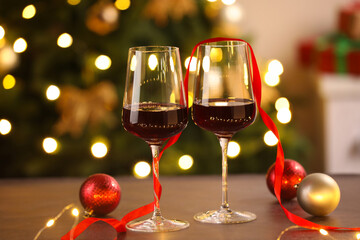 Fototapeta premium Glasses of red wine and Christmas decor on wooden table against background with blurred lights