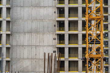 Close-up view of unfinished concrete high-rise building under construction, revealing raw structural elements, yellow safety railings, and prominent tower crane on developing urban site.