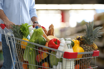 Man with shopping cart full of products in supermarket, closeup