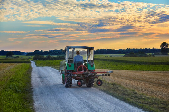 Farmer drives home in his old tractor at sunset. In Germany.