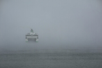 Ferry moving into dense fog over calm water.