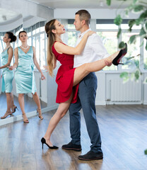 Fototapeta premium Guy and girl in stage costumes, under guidance of mentor, practice tango in choreographic studio. Ballet dancers during personal training session. Professional rendering of dance entertainment