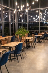 Fototapeta premium Interior view of a modern restaurant at night featuring wooden tables, mixed beige and blue chairs