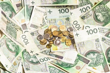 A scattered pile of Polish 100-zloty banknotes with small 1, 2, 5, and 10-grosz coins placed in the...