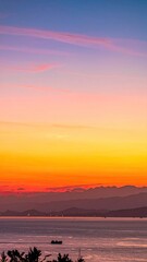 Vivid sunset colors over ocean, with hazy mountains and a boat silhouette