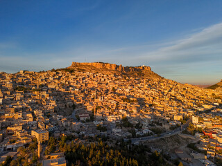 Captivating aerial view of Old Mardin during golden hour. The historic stone city glows with warm...