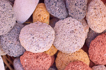 Colorful volcanic pumice stones in various shades are arranged together, showcasing their unique textures and porous surfaces, ideal for natural beauty and wellness applications