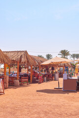Vibrant outdoor market scene featuring straw-roofed stalls, colorful crafts, and palm trees under a clear blue sky, showcasing a lively atmosphere and cultural richness