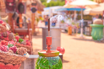 Colorful incense holder with smoke rising, surrounded by vibrant flowers and decorative items in a lively outdoor market setting, showcasing cultural ambiance and craftsmanship