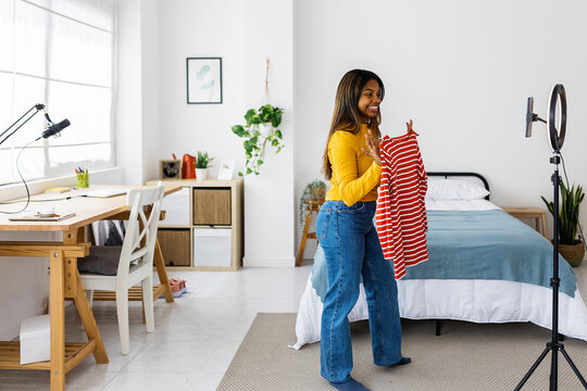 Young woman presenting clothing items, recording video for her fashion blog in a home studio