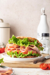 Delisious sandwich with ham lettuce tomatoes and grilled bread for breakfast on beige kitchen table