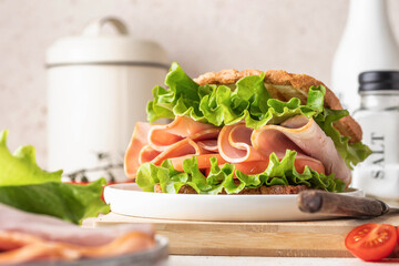 Delisious sandwich with ham lettuce tomatoes and grilled bread for breakfast on beige kitchen table