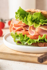 Delisious sandwich with ham lettuce tomatoes and grilled bread close up for breakfast on beige kitchen table