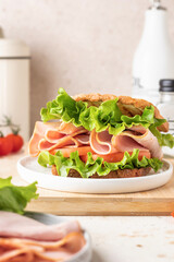 Delisious sandwich with ham lettuce tomatoes and grilled bread for breakfast on beige kitchen table