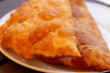 Hearty lunch: Chebureks with meat on a white plate on a wooden table. Big chebureks for dinner. Meat pies. Close-up.