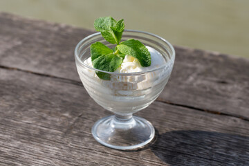 Delicious butter ice cream in a glass bowl with green mint on a wooden board, close-up.