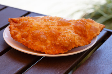 Hearty lunch: Chebureks with meat on a white plate on a wooden table. Big chebureks for dinner. Meat pies. Close-up.