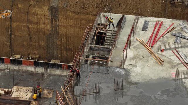 Aerial close up of construction workers reinforcing concrete foundation walls with rebar and formwork inside a deep excavation