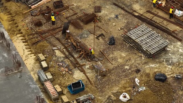 Aerial close up of construction workers handling metal rebar and formwork materials on a muddy building site