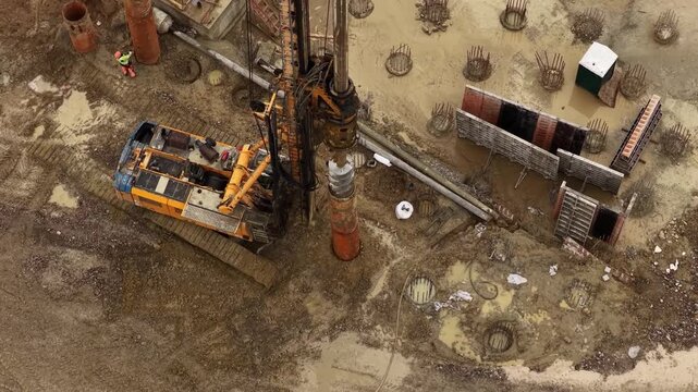 Drilling rig lowering auger into casing pipe at muddy construction foundation