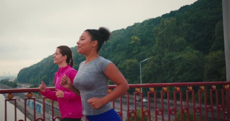 Woman athletes run side by side across pedestrian bridge