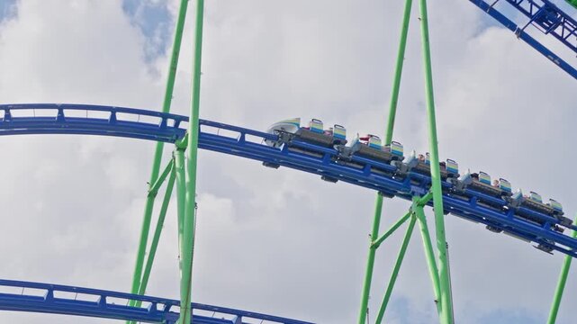 roller coaster riders cresting blue track green steel supports, cars packed with excited passengers, hands raised, joyful screams, high-altitude curve, bright summer sky, cinematic framing