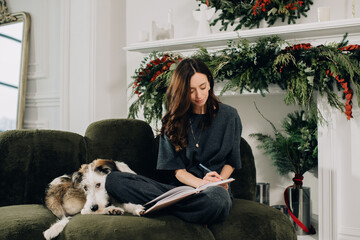 Woman writing next to dog on christmas sofa