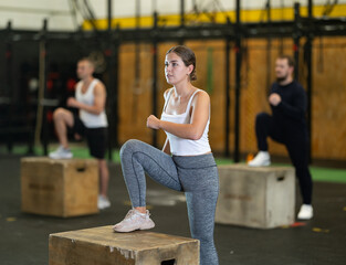 Sportive young woman doing step-up exercises with box in gym during training session