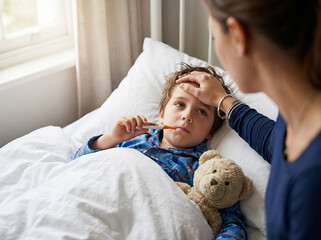 Childhood illness and fever concept with loving mother caring for her sick son in bed and checking his temperature.