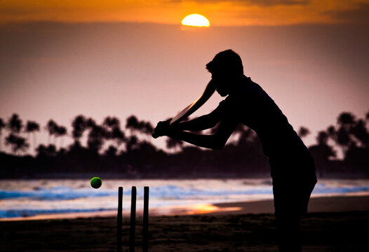 Boy playing cricket at sunset on tropical beach in Sri Lanka