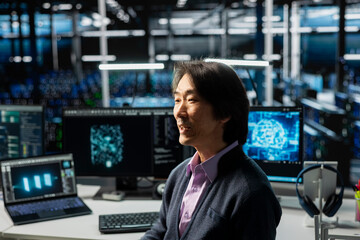 System administrator in data center using PC, managing AI training datasets. Asian man using computer program to oversee machine learning in server room supporting scalable infrastructure for AI apps