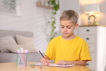 Cute little boy drawing at wooden table indoors. Space for text