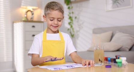Cute little boy painting his handprint at wooden table indoors. Space for text