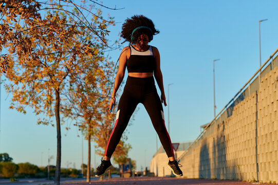 Sport woman jumping while listening music with headphones in the city during sunset