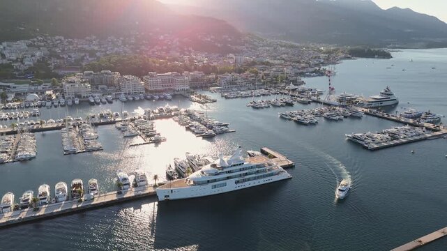 Luxury yacht leaving Porto Montenegro marina in Tivat, Montenegro &ndash; aerial 4K drone view with superyacht in foreground and luxury waterfront marina with moored boats in the background.