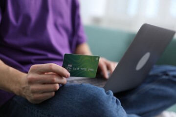Young man making online payment with laptop and credit card indoors, closeup