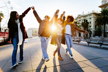 Happy group of young people having fun together walking in Barcelona city. Joyful diverse friends holding hands celebrating outdoors. Youth, friendship and travel concept.