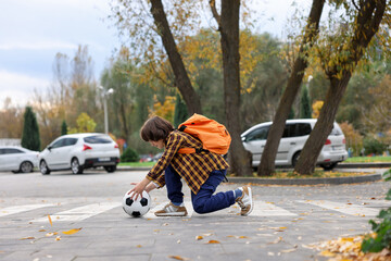 Little boy with backpack catching ball on pedestrian crossing outdoors. Child in danger and road safety